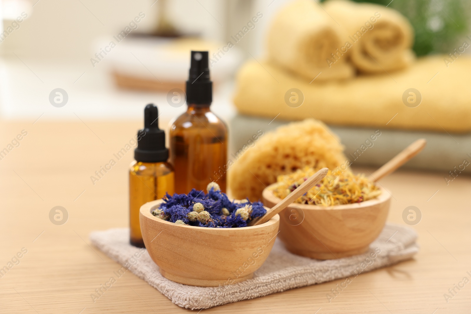 Photo of Bottles of essential oils, bowls with dry flowers and natural sponge on light wooden table, closeup. Spa therapy