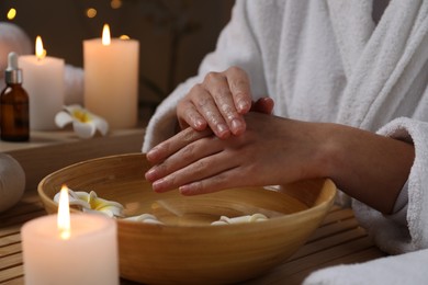 Woman soaking her hands in bowl of water and flowers at table, closeup. Spa treatment