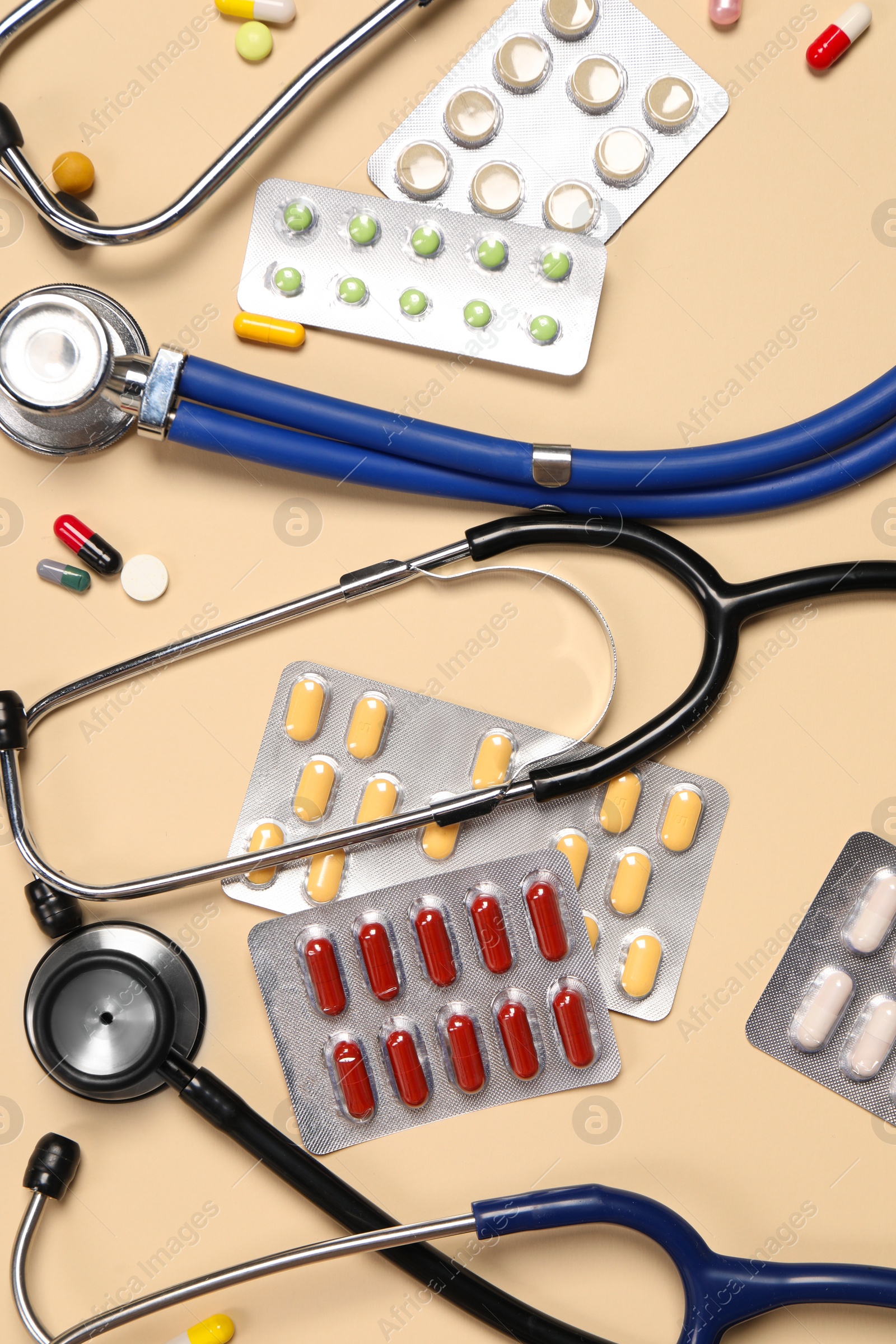 Photo of Stethoscopes and pills on beige background, flat lay. Medical tools