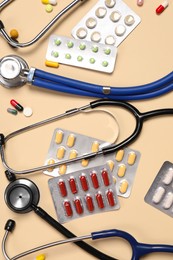 Photo of Stethoscopes and pills on beige background, flat lay. Medical tools