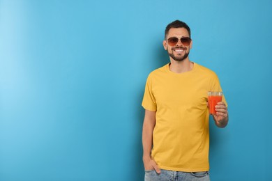 Photo of Man holding glass of delicious juice on light blue background, space for text