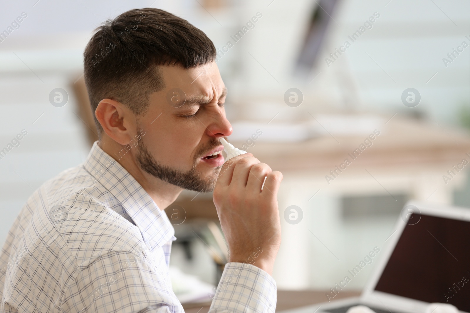 Photo of Ill man using nasal spray in office