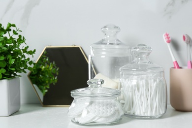 Jars with cotton swabs and pads on white countertop in bathroom
