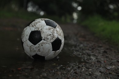 Dirty leather soccer ball in puddle outdoors