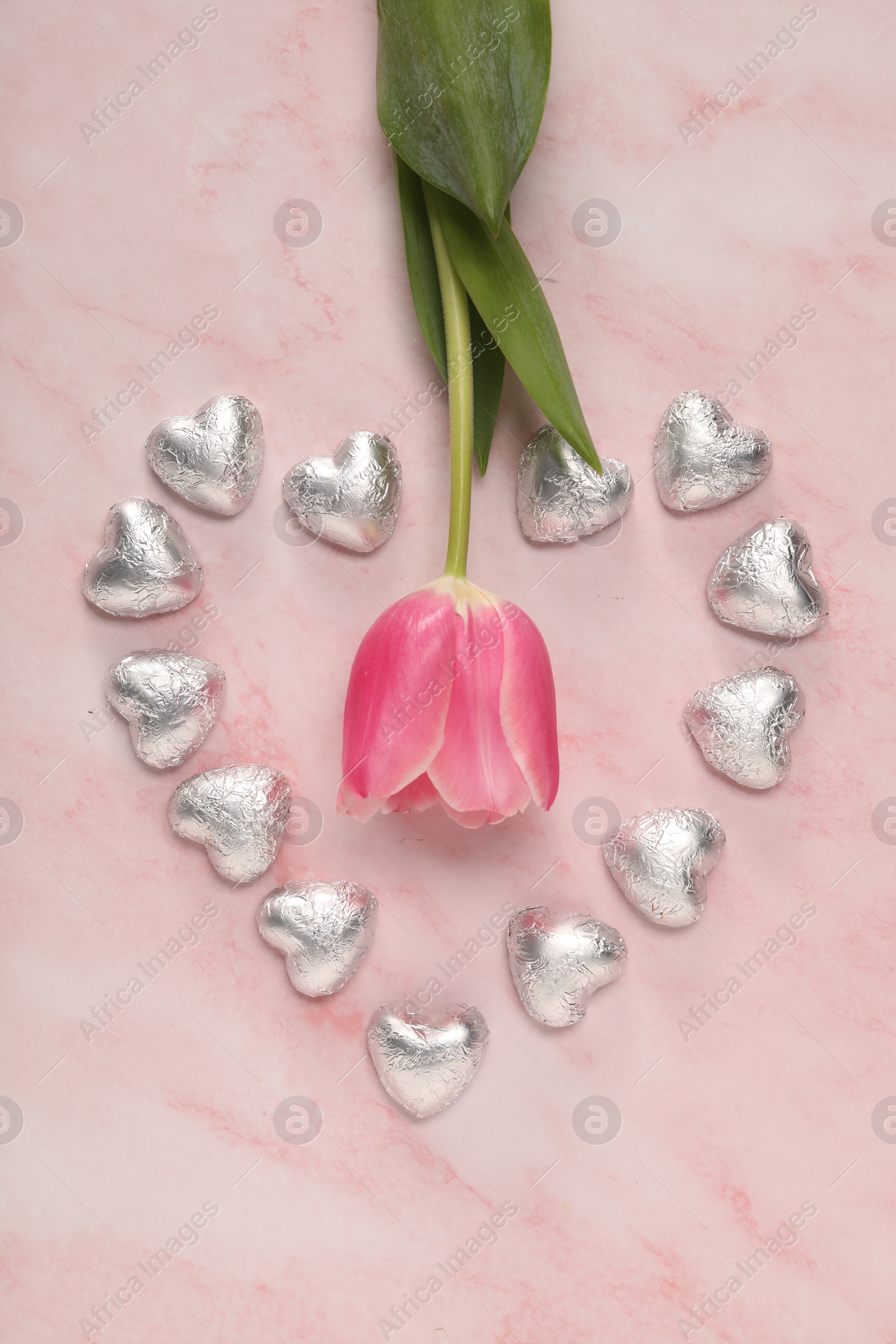 Photo of Heart made with delicious chocolate candies and beautiful tulip on pink table, flat lay