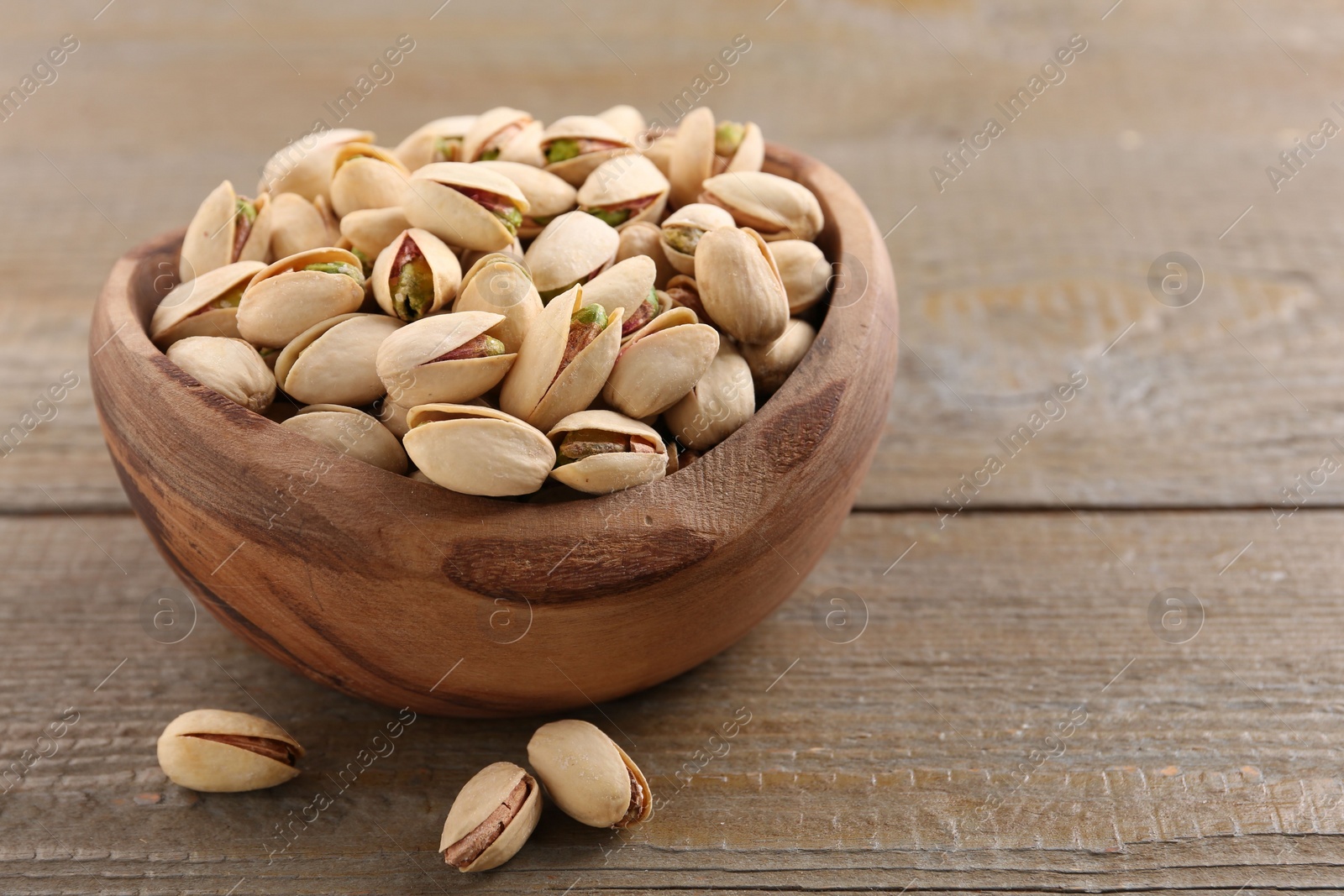 Photo of Delicious pistachios in bowl on wooden table. Space for text