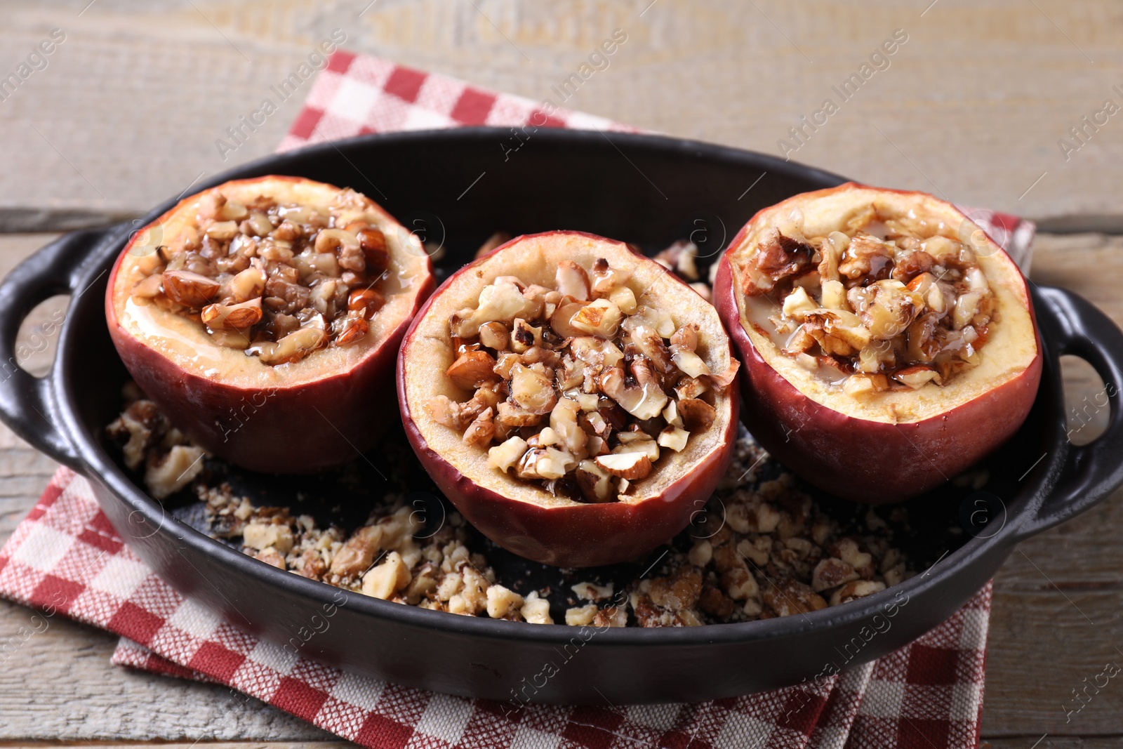 Photo of Tasty baked apples with nuts and honey in baking dish on wooden table, closeup