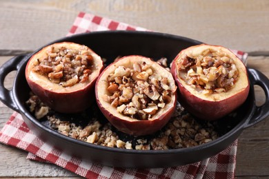 Photo of Tasty baked apples with nuts and honey in baking dish on wooden table, closeup