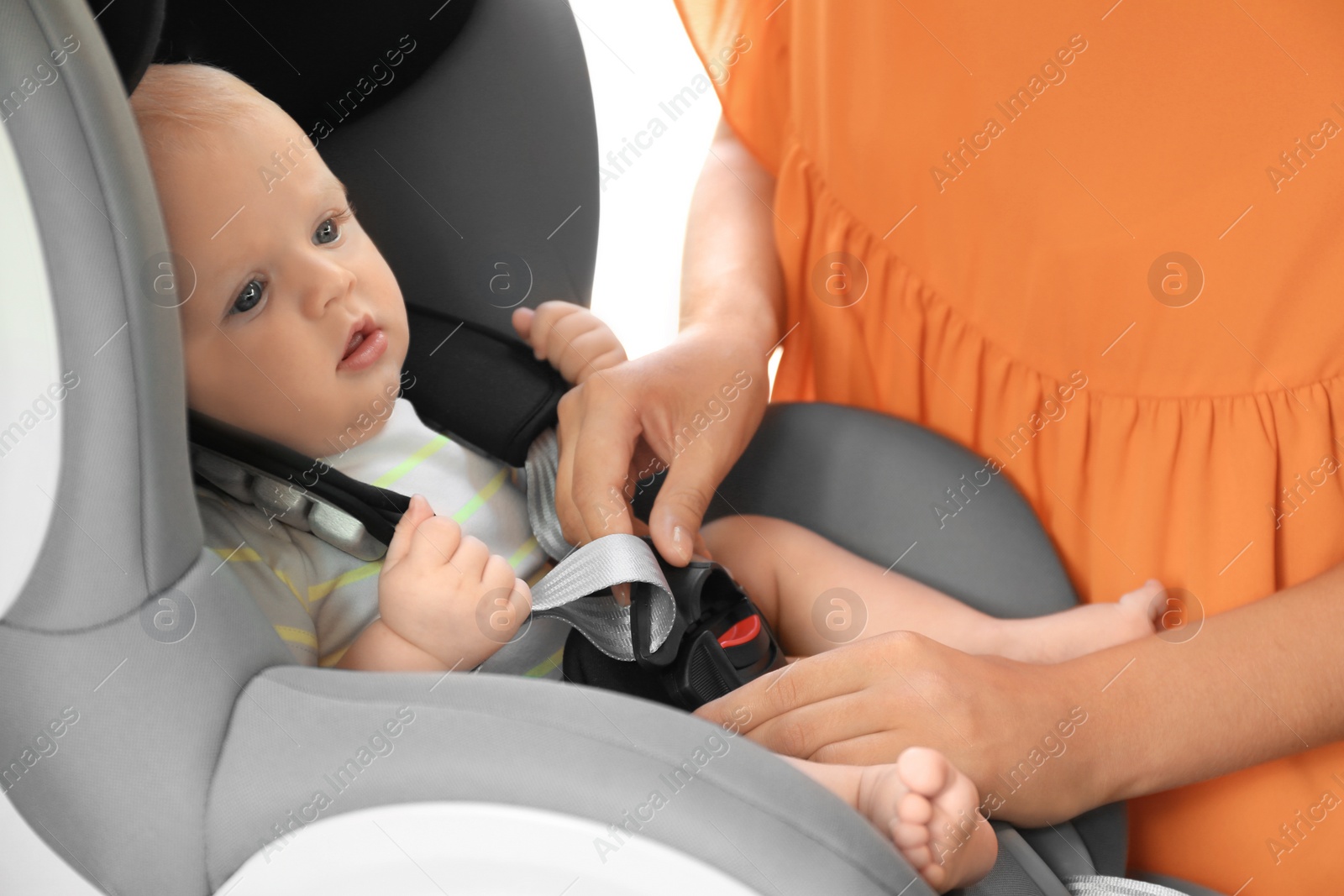 Photo of Mother fastening baby to child safety seat inside of car