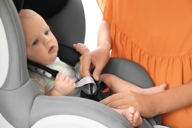 Mother fastening baby to child safety seat inside of car