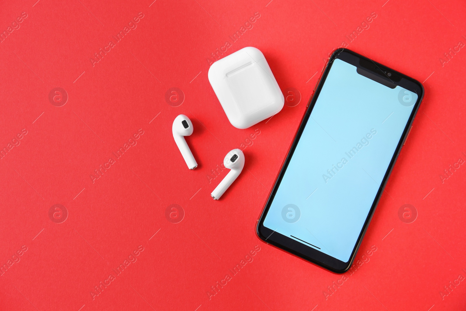 Photo of Wireless earphones, mobile phone and charging case on red background, flat lay. Space for text