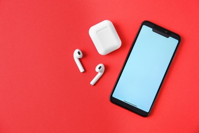 Photo of Wireless earphones, mobile phone and charging case on red background, flat lay. Space for text