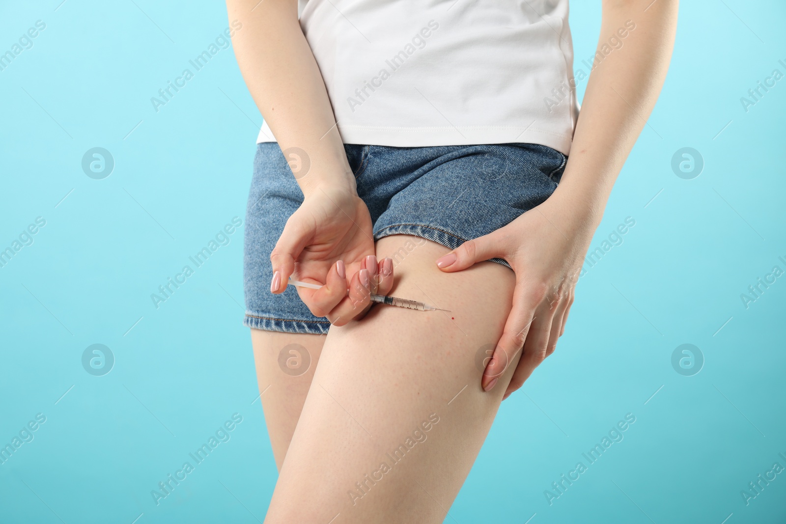 Photo of Diabetes. Woman making insulin injection into her leg on light blue background, closeup