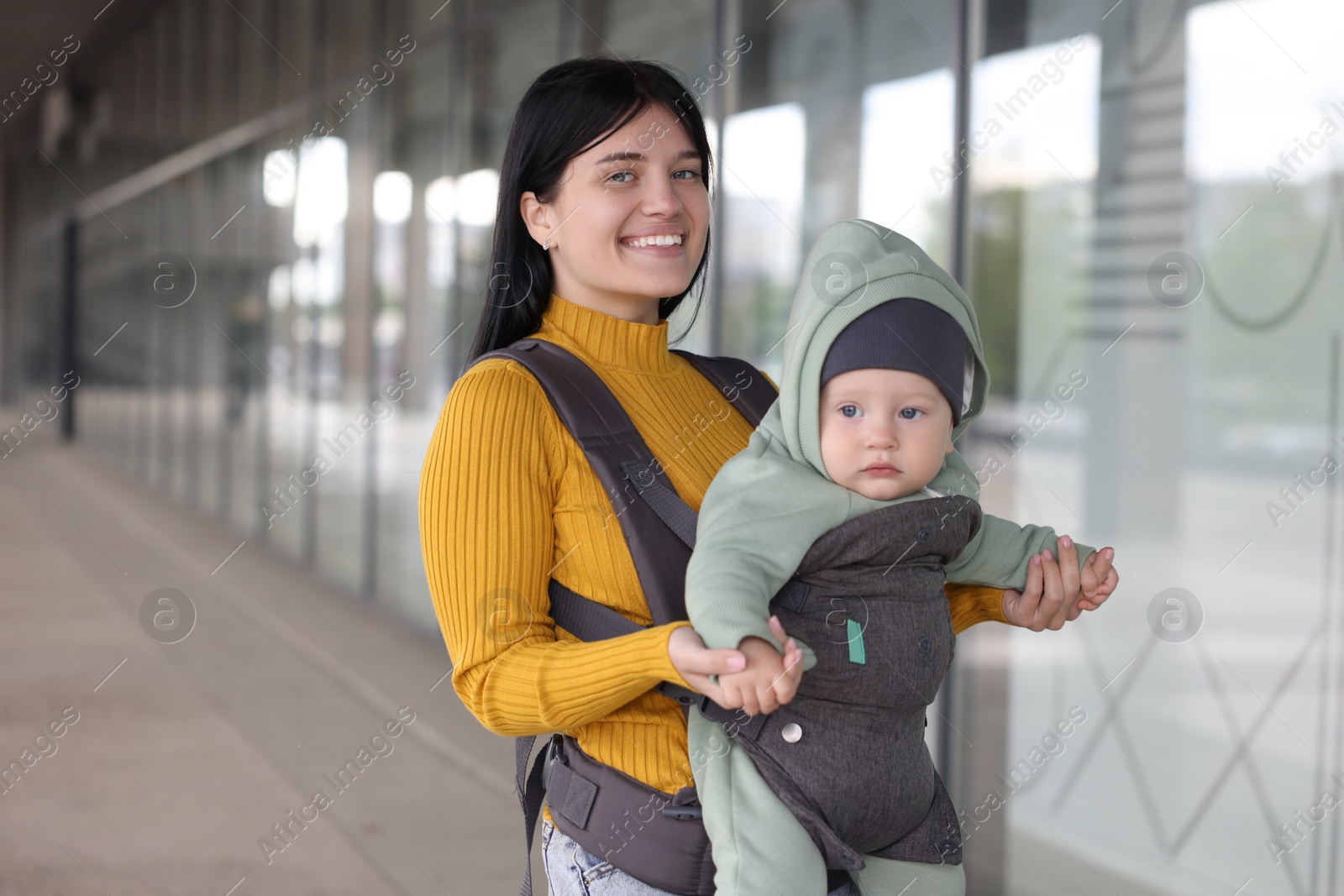 Photo of Mother holding her child in sling (baby carrier) near building outdoors