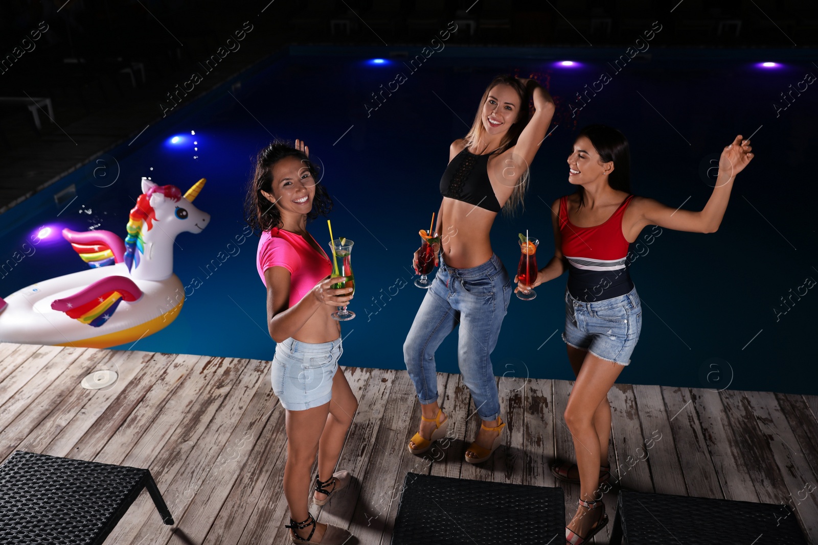 Photo of Happy young friends with refreshing cocktails relaxing near outdoor swimming pool at night