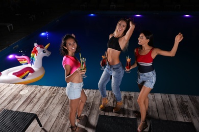Photo of Happy young friends with refreshing cocktails relaxing near outdoor swimming pool at night