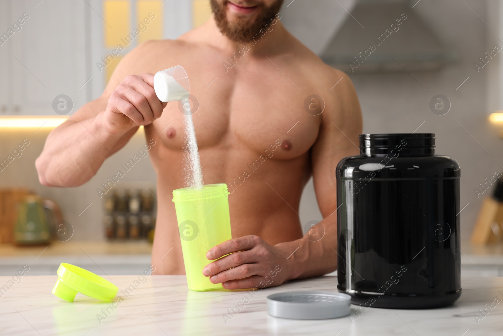 Photo of Young muscular man making protein shake at white marble table in kitchen, focus on jar