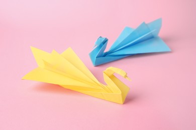 Photo of Origami art. Beautiful paper swans on pink background