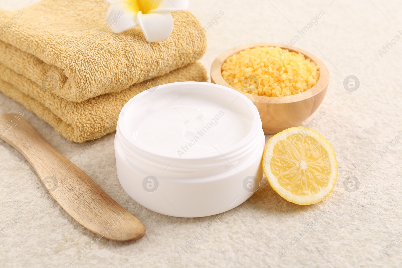 Photo of Body care. Composition with moisturizing cream in open jar and half of lemon on light textured table, closeup