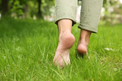 Photo of Woman walking barefoot on green grass outdoors, closeup