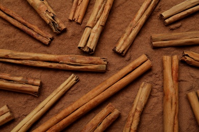 Photo of Many cinnamon sticks on powder, flat lay