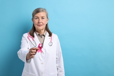 Photo of Mammologist with pink ribbon on light blue background, space for text. Breast cancer awareness