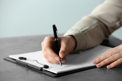 Photo of Woman writing in documents with pen at grey table, closeup
