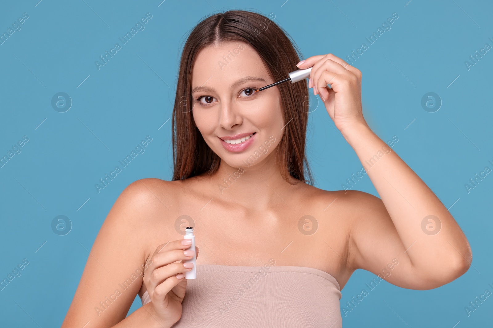 Photo of Beautiful woman applying serum onto eyelashes on light blue background