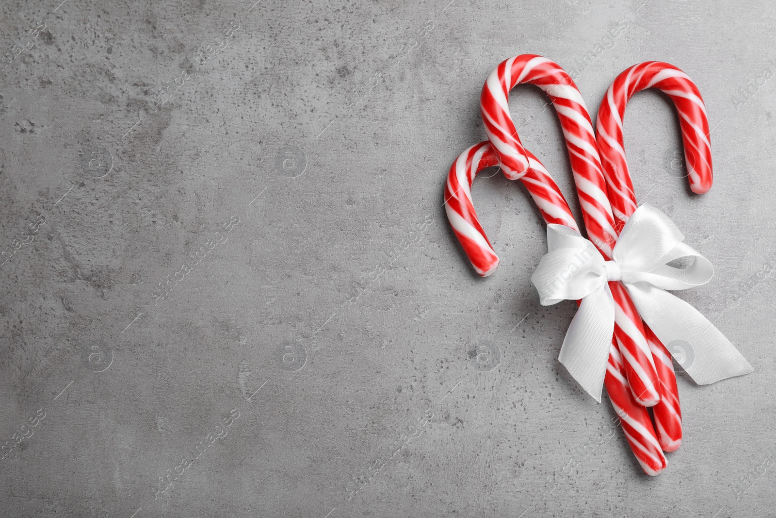 Photo of Sweet Christmas candy canes with white bow on grey background, top view. Space for text