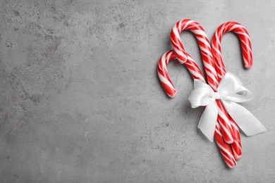 Photo of Sweet Christmas candy canes with white bow on grey background, top view. Space for text
