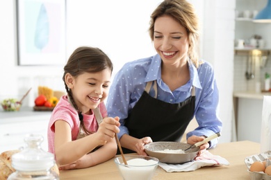 Young nanny with cute little girl cooking together in kitchen