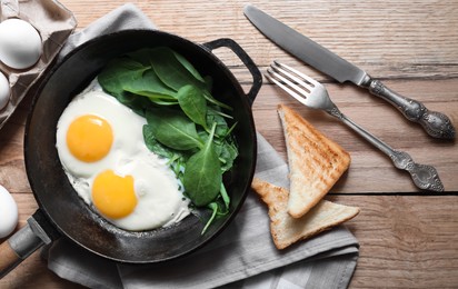 Delicious fried egg with spinach served on wooden table, flat lay
