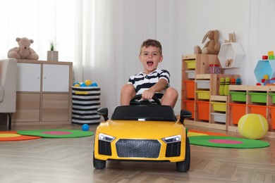 Emotional little boy driving big toy car at home