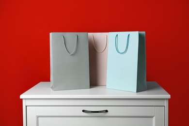 Photo of Paper shopping bags on white chest of drawers against red background