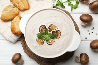 Delicious homemade mushroom soup in ceramic pot, croutons, fresh champignons and parsley on white wooden table, flat lay