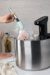 Photo of Woman putting vacuum packed meat into pot with sous vide cooker at table, closeup. Thermal immersion circulator