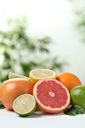 Photo of Different fresh citrus fruits and leaves on white table against blurred background. Space for text