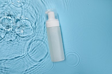 Bottle of face cleansing product in water against light blue background, top view