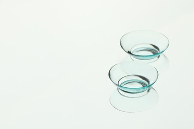 Photo of Pair of contact lenses on white reflective surface. Space for text