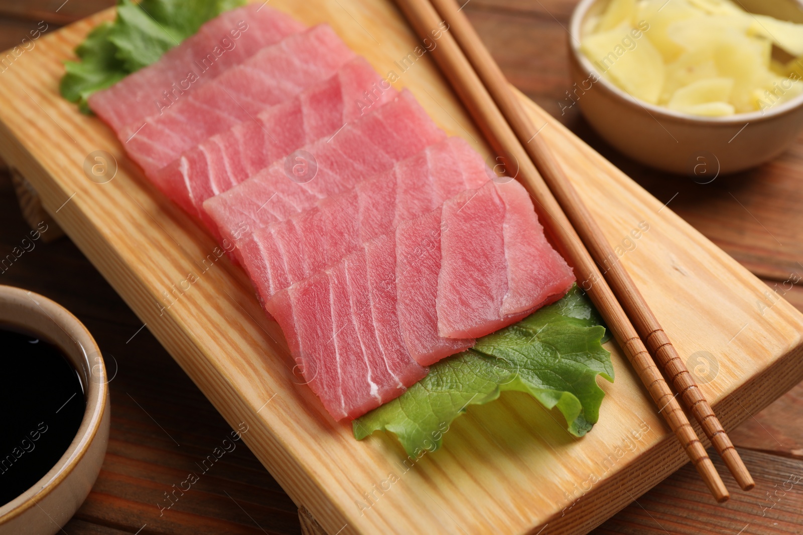 Photo of Tasty sashimi (pieces of fresh raw tuna), lettuce and chopsticks on wooden board