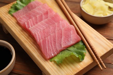 Photo of Tasty sashimi (pieces of fresh raw tuna), lettuce and chopsticks on wooden board