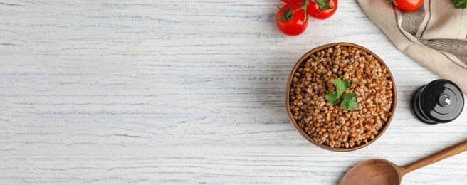 Flat lay composition with bowl of buckwheat porridge served on white wooden table, space for text. Banner design