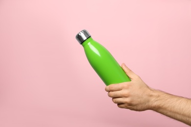 Photo of Man holding green thermos bottle on pink background, closeup
