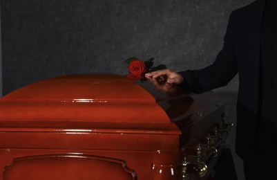 Photo of Young man near casket with red rose in funeral home, closeup