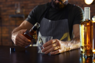 Photo of Bartender pouring whiskey into glass at counter in bar, closeup