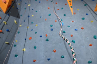 Climbing wall with holds and ropes in gym, low angle view. Extreme sport