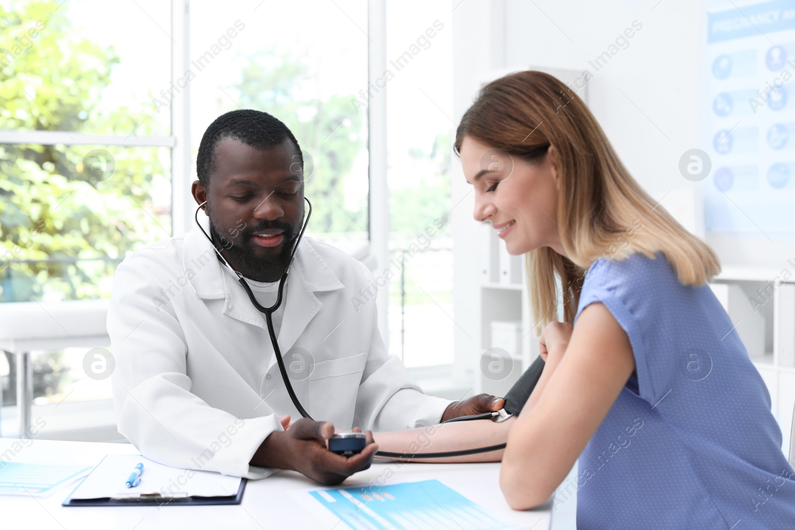 Photo of Young African-American doctor checking patient's pulse and blood pressure in hospital