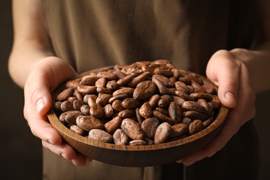 Photo of Woman holding wooden bowl of cocoa beans, closeup view