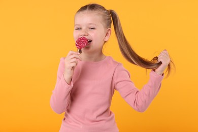 Photo of Happy little girl with bright lollipop swirl on orange background