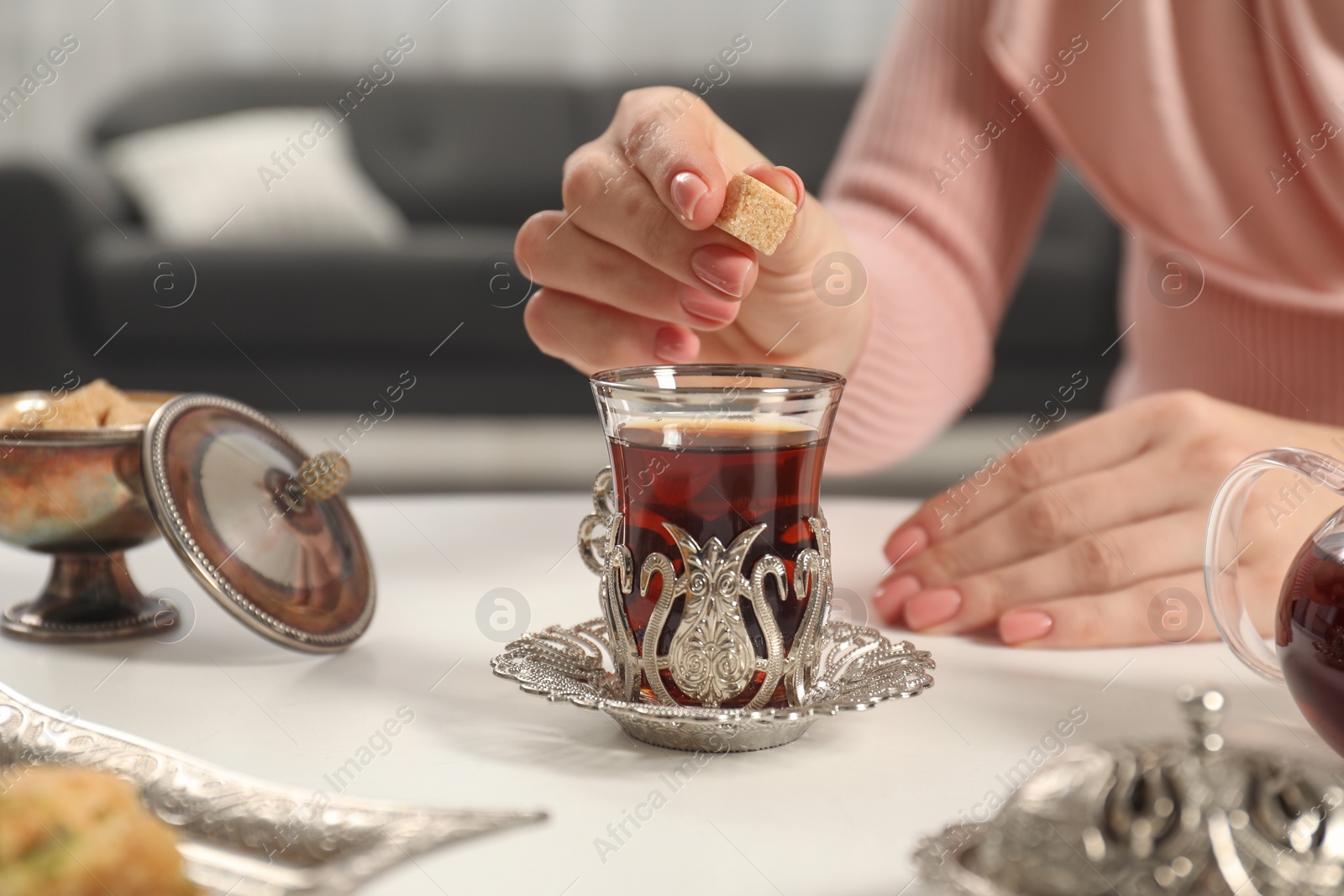 Photo of Woman adding sugar to delicious Turkish tea at white table, closeup